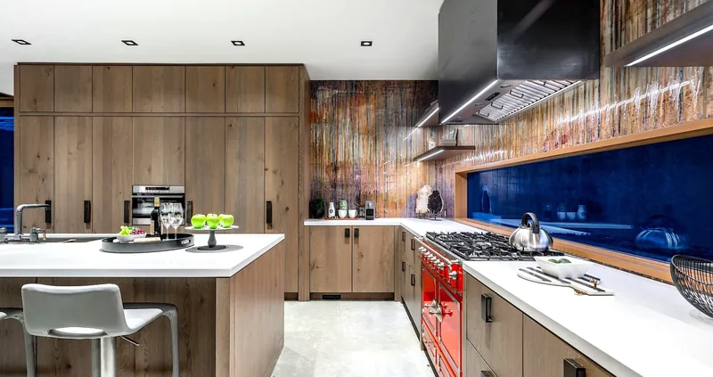 A designer kitchen in natural wood cabinetry with a red La Cornue range, white quartz counters and a navy backsplash.