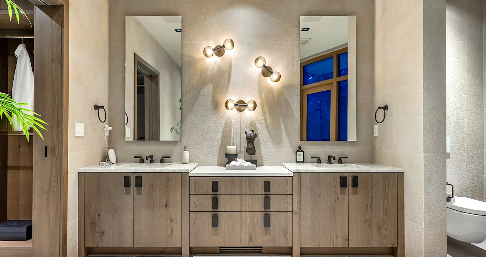 A Zen-inspired Kerrisdale master ensuite: dual under-mount sinks, black fixtures, natural wood cabinetry and sculptural wall sconces.