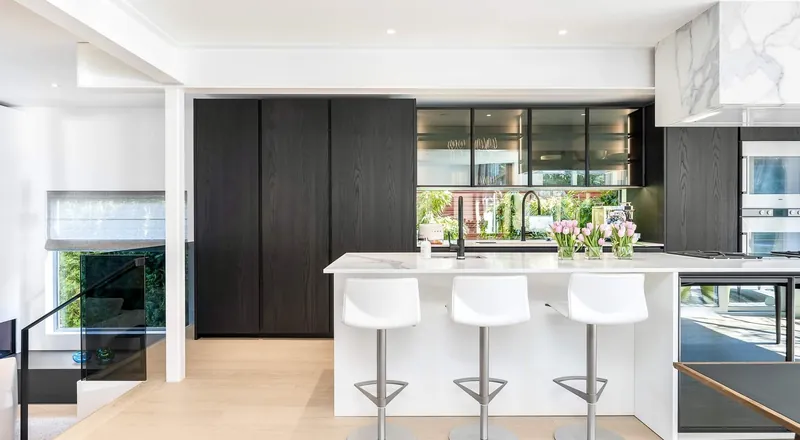 A kitchen island with white bar stools in front of dark full-height cabinetry and a glazed wall.