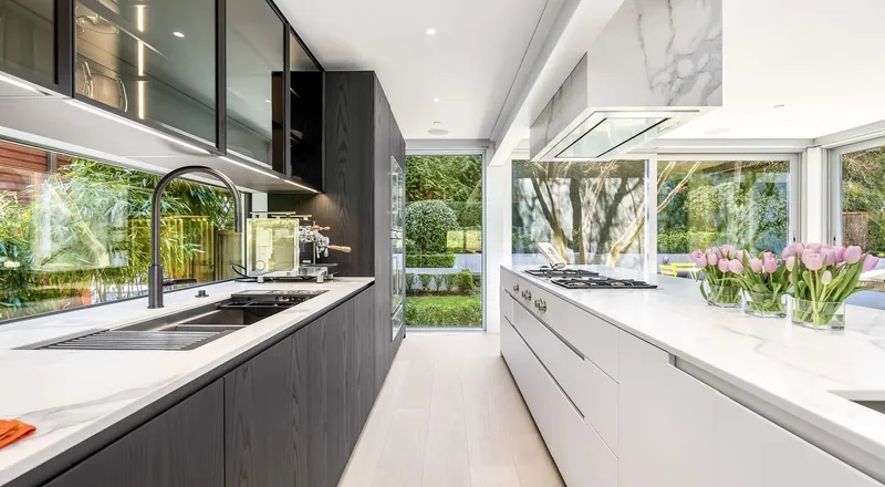 A galley kitchen with dark cabinetry on one side and white counters under windows on the other.
